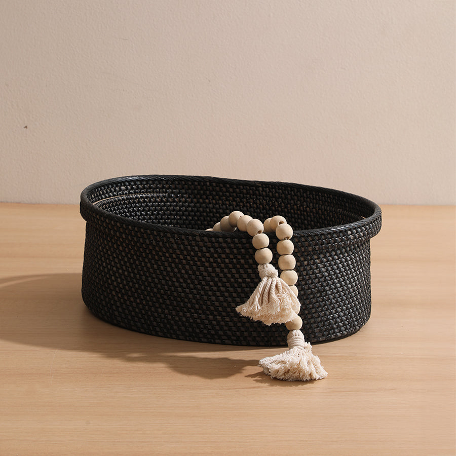 Black woven basket, Decorative storage basket, Round wicker bin, Handwoven black basket, Rattan organizer basket, Black decorative basket with tassel accents, Handcrafted round basket for tabletop storage, Woven black storage bin for minimalist décor, 
Rustic black basket with Boho bead garland, Boho farmhouse storage basket, Minimalist home décor basket, Black rattan catchall tray, 
Neutral-toned basket for modern homes, Functional and decorative black organizer .
