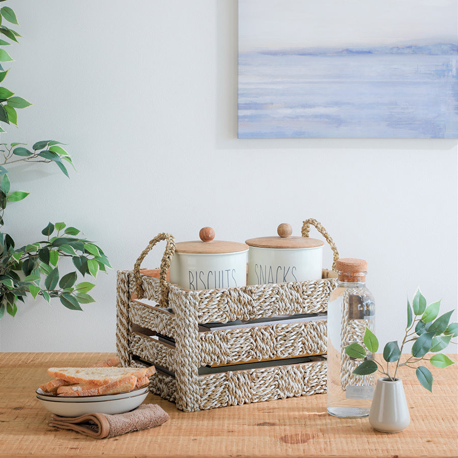 Seaweed rope basket, Handwoven storage crate, Natural woven organizer, Ceramic kitchen canisters,
Snack and biscuit storage jars,
Airtight ceramic containers with wooden lids, Ceramic breakfast bowl,
Rustic ceramic bowl set, Farmhouse style kitchen jars, Clear glass water bottle, Minimalist glass carafe with cork top, Small ceramic bud vase,
Faux greenery in vase.