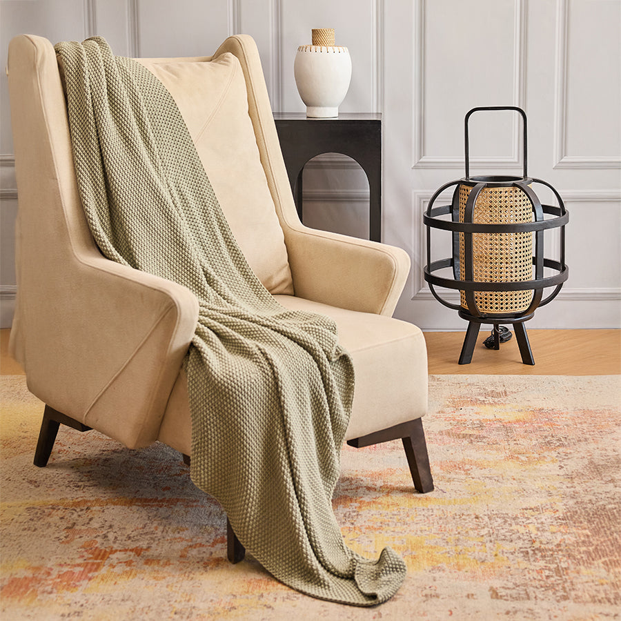 beige wingback accent chair, modern lounge armchair, upholstered reading chair, sage green throw blanket, chunky knit couch throw, textured throw for sofa, rattan table lamp, black cage woven lantern,
industrial rattan accent lamp.