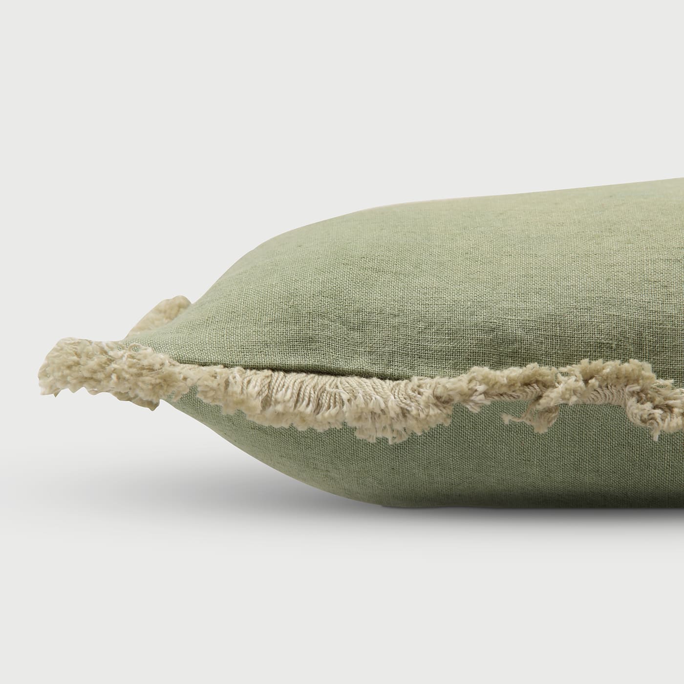 Green cushion with fringe trim
Side view of linen pillow, Soft green throw cushion, Fringed edge cushion cover, Natural fiber cushion, Minimalist fringe pillow, Handcrafted cushion side profile, Vintage-inspired throw pillow, Artisan made green cushion, Neutral tone cushion décor. 
Earthy green home accessory.