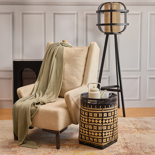 Wingback lounge chair, Neutral upholstered armchair, Soft fabric reading chair, Comfortable armchair with high back, Black and natural rattan bin, Decorative side table basket, Ethnic pattern woven storage, Multipurpose tribal basket table.

