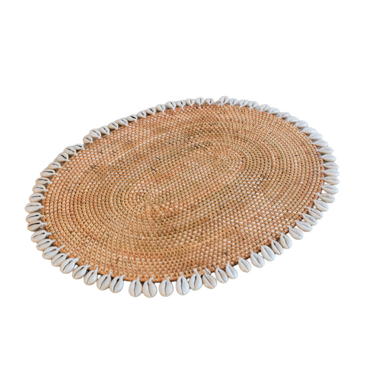 Cowrie shell placemat, Handmade woven placemat, Natural rattan table mat, Boho coastal table décor, Oval jute placemat, Bohemian dining table accessories, Handcrafted placemat with shells, Eco-friendly rattan table mat, Beach-themed placemat décor, Rustic shell-edge placemat. 